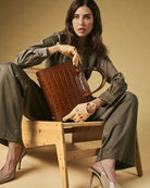 Woman holding a brown leather handbag in a studio setting