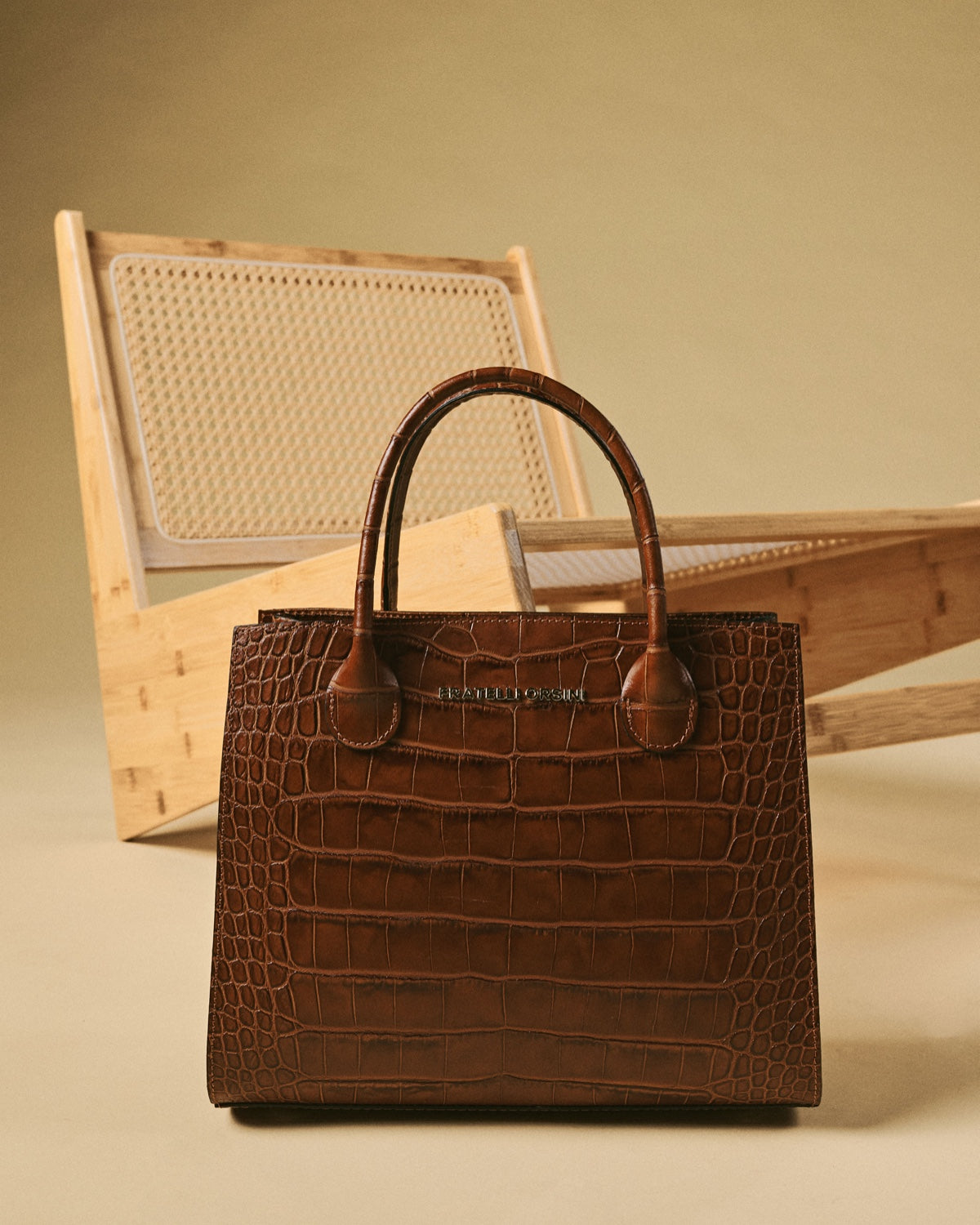 Brown crocodile-patterned handbag on a beige surface with a wooden chair in the background