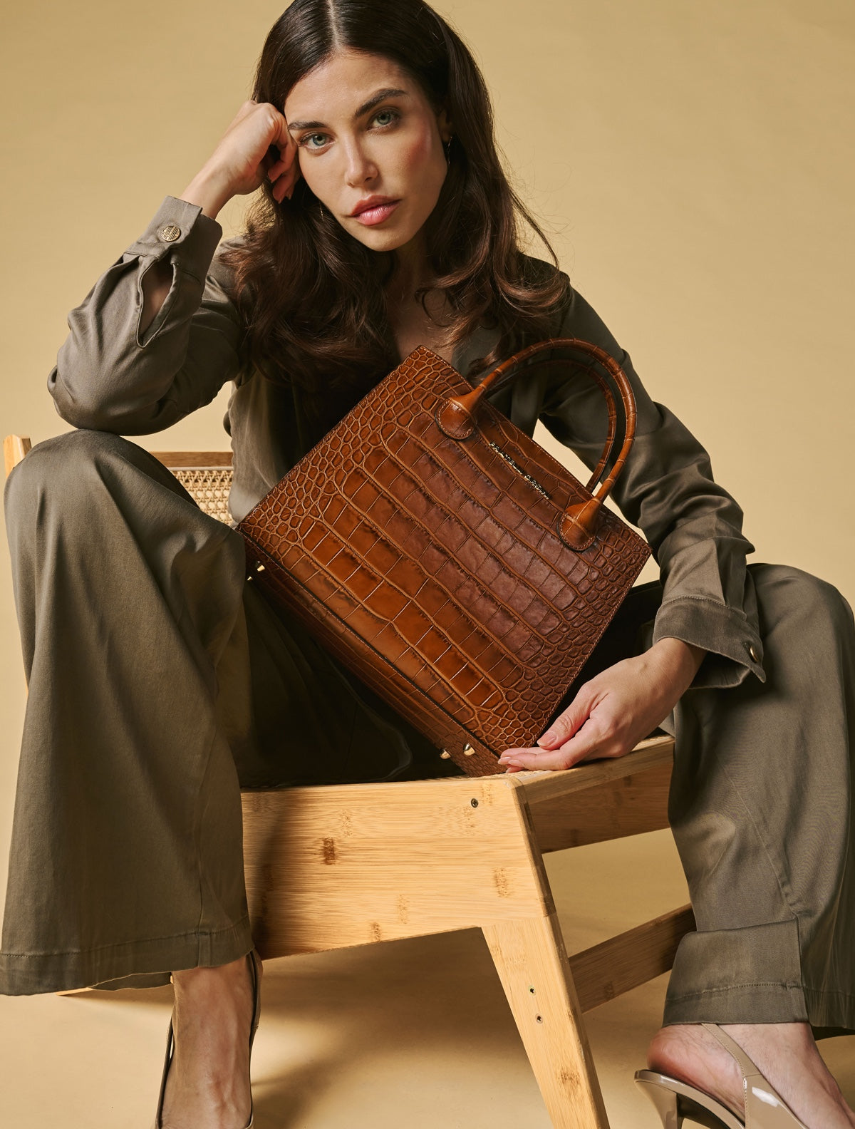 Woman holding a brown leather handbag in a studio setting