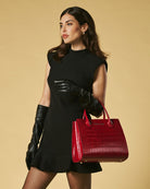 Woman in black dress and gloves holding a red handbag against a beige background