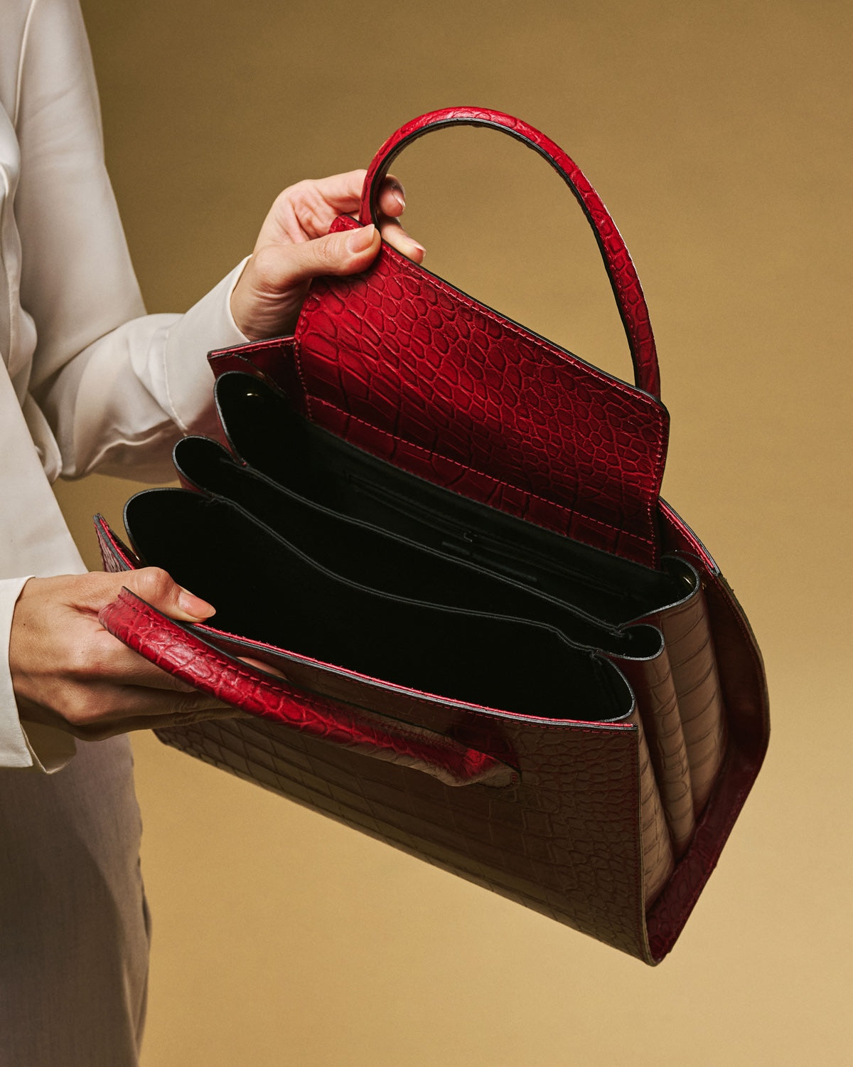 Red handbag with a textured surface held by a person against a beige background