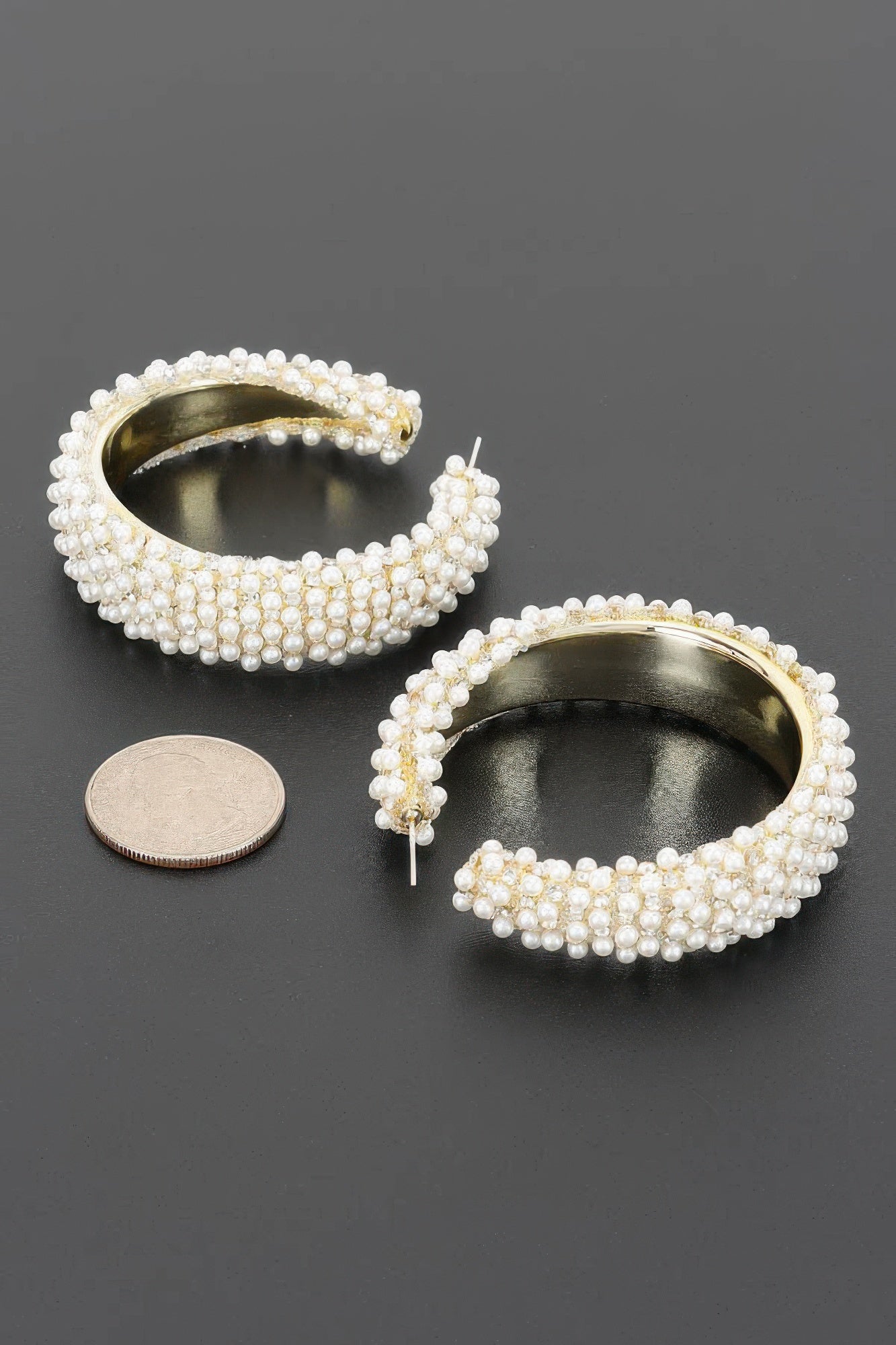 Angled view of Pearl Reverie Statement Hoop Earrings showing pearl detailing, gold tone interior and post closures.