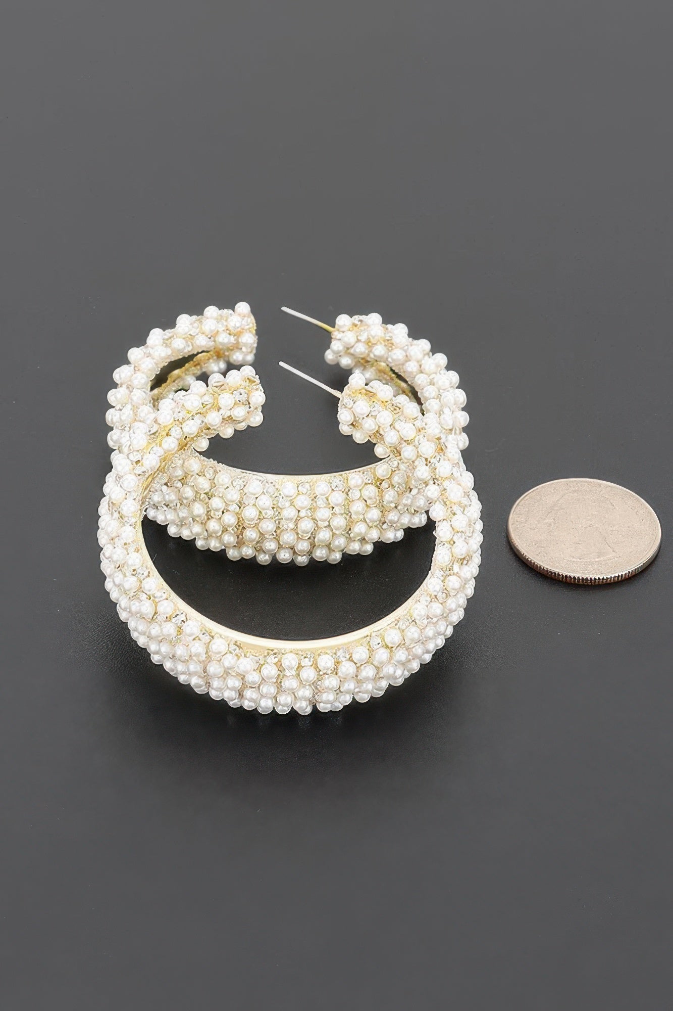 Pearl Reverie pearl encrusted hoop earrings shown with coin for size reference.