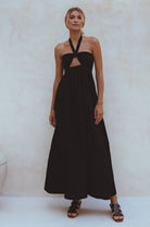 Woman wearing a black linen maxi dress with halter neck and front cut out against a plain background
