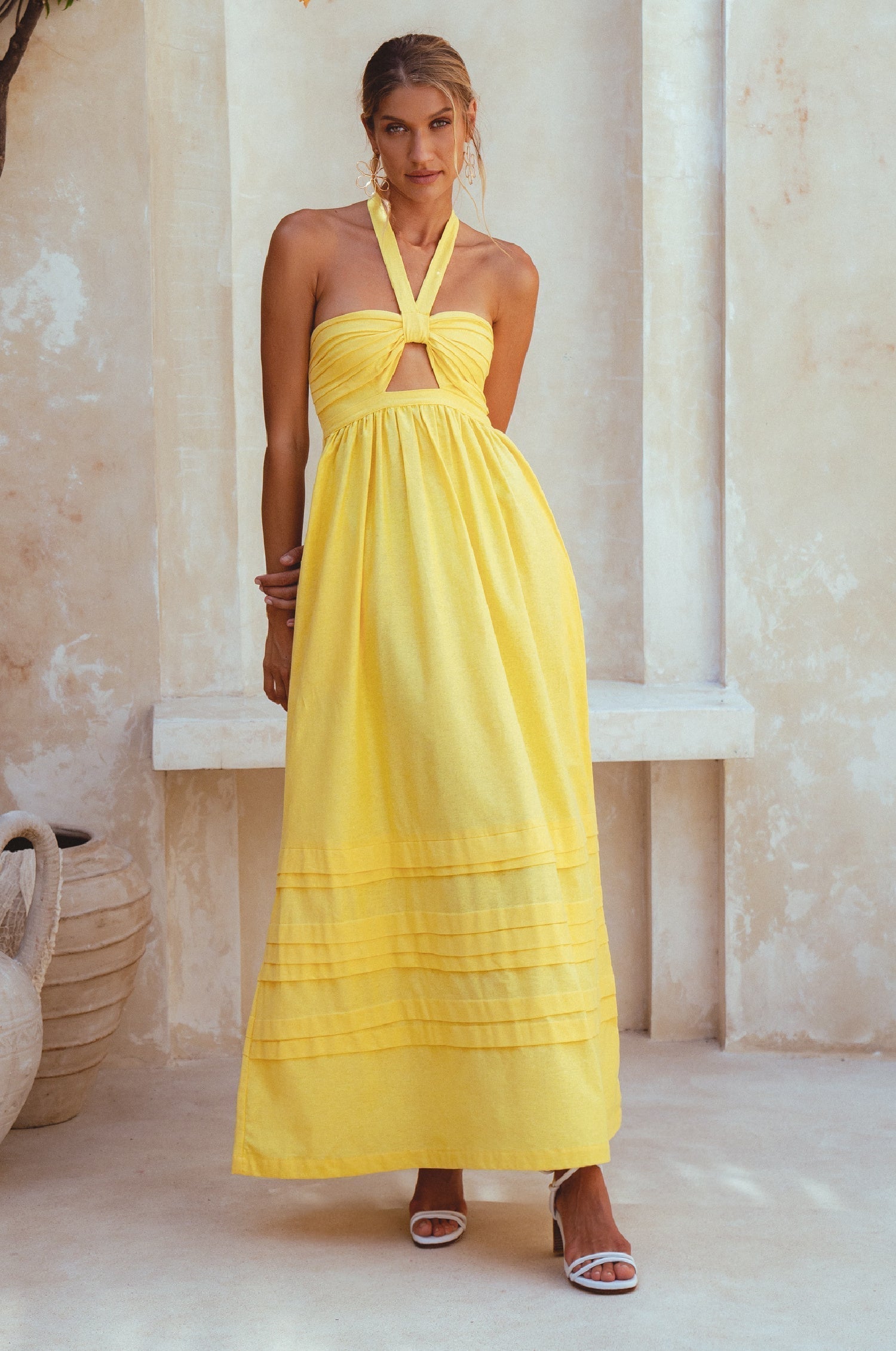 Woman wearing a yellow halter neck dress standing in a sunlit room with columns.