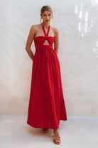 Woman wearing a red linen maxi dress with halter neck and front cut out against a white background