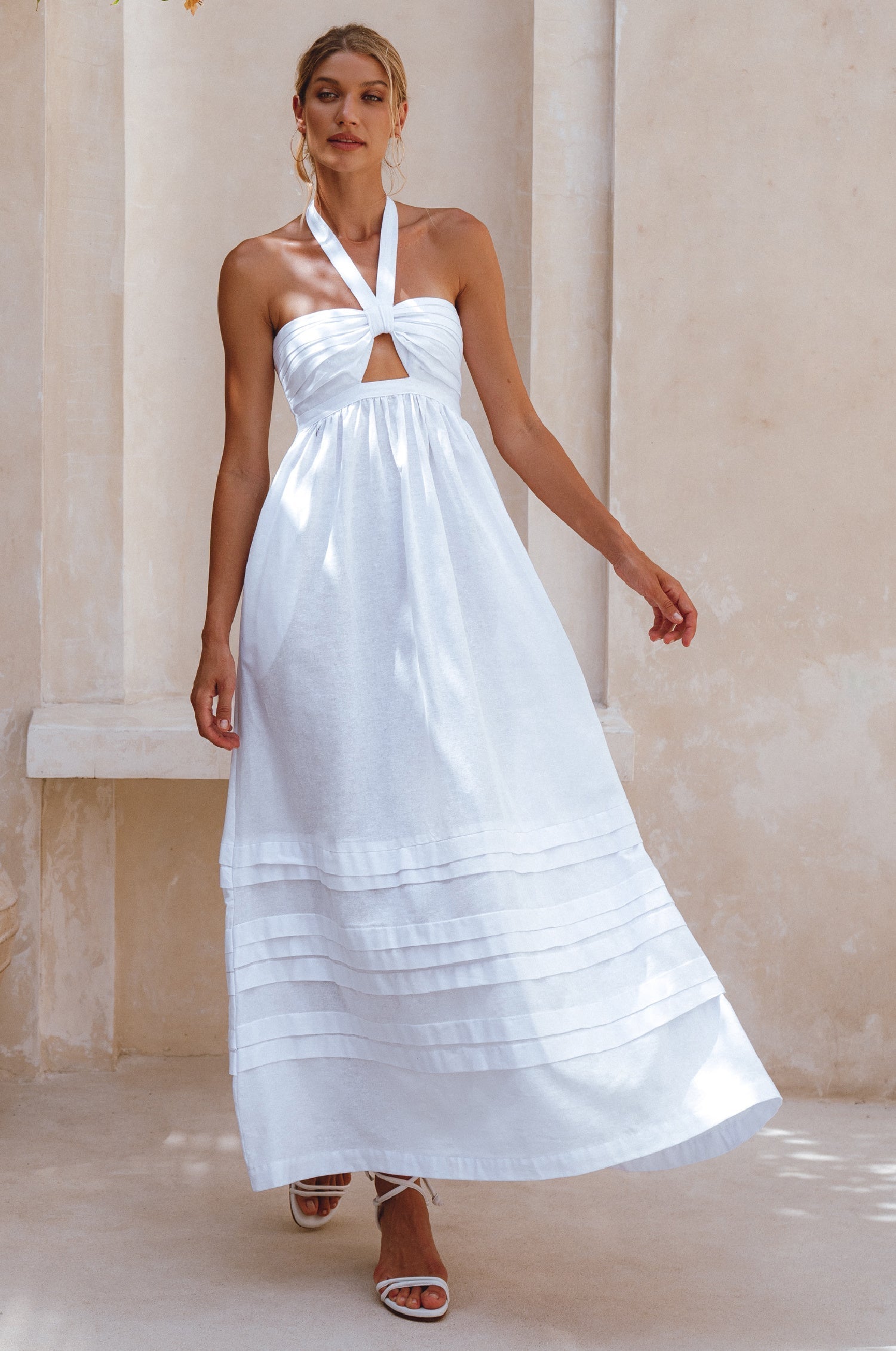 Woman wearing a white halter neck dress standing against a neutral background
