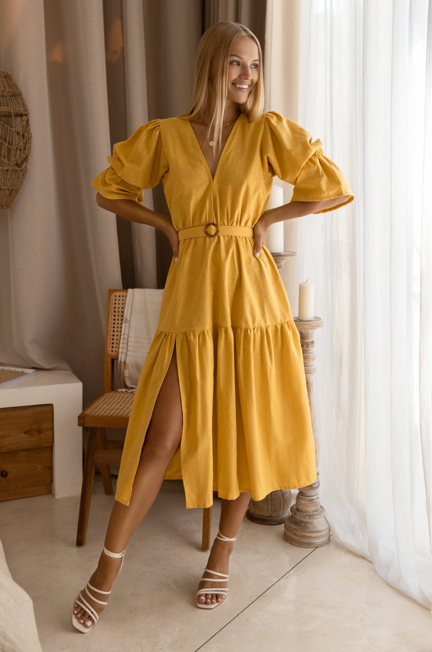 Woman wearing a yellow dress in a room with curtains and furniture.