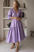 Woman wearing a purple dress standing in a room with shelves.