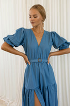 Woman wearing a blue dress with ruffled sleeves against a white curtain background