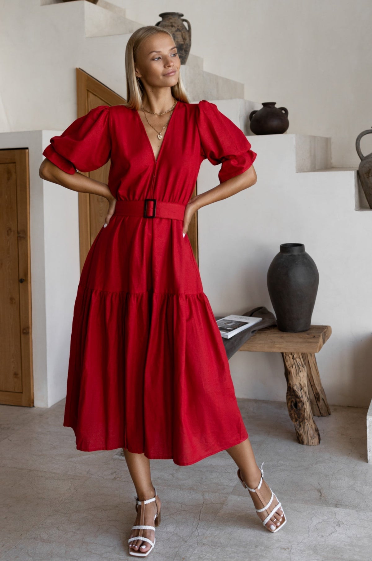 Woman in a red dress standing in a room with white walls and wooden furniture.