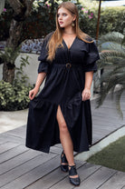 Woman wearing a black dress with a belt standing on a wooden deck.