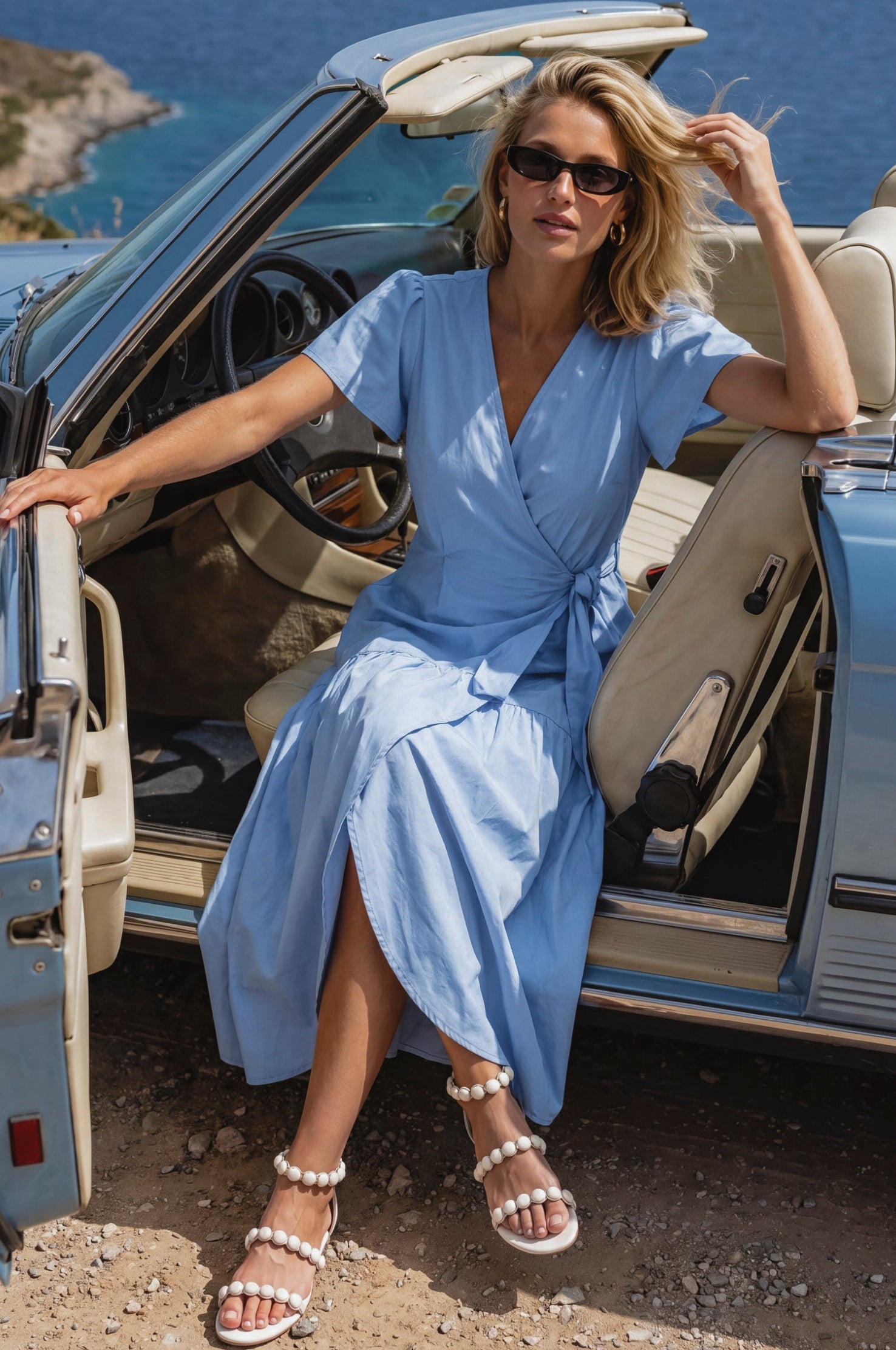 Woman in a blue wrap midi dress sitting in an open car with a scenic background