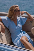 Woman in a blue dress sitting in a convertible car by the ocean