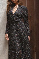 Woman wearing a black floral dress against a textured wall.