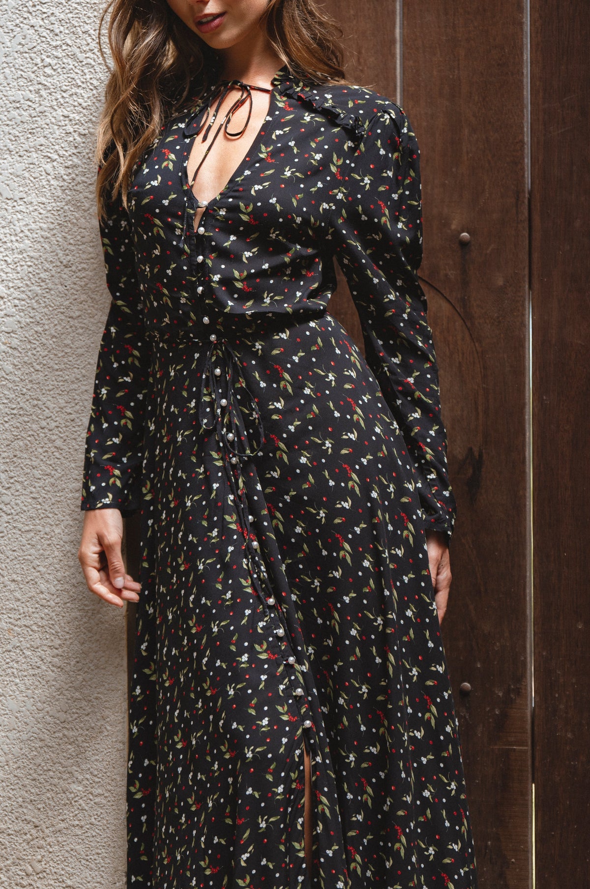 Woman wearing a black floral dress against a textured wall.