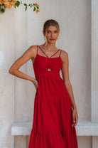 Model wearing a red linen tiered midi dress with dual adjustable spaghetti straps standing against a light-colored wall