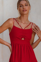 Woman wearing a red linen tiered midi dress with dual adjustable spaghetti straps standing against a light-colored wall, close up of bodice.
