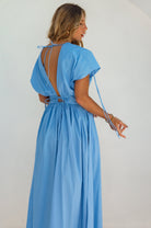 Woman wearing a blue maxi dress sleeves un-gathered and backless design on a white background