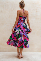 Woman wearing a colorful halter tiered mid dress with a neutral background back view