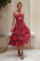 Woman wearing a red floral halter tiered midi dress standing in a decorative setting, front view