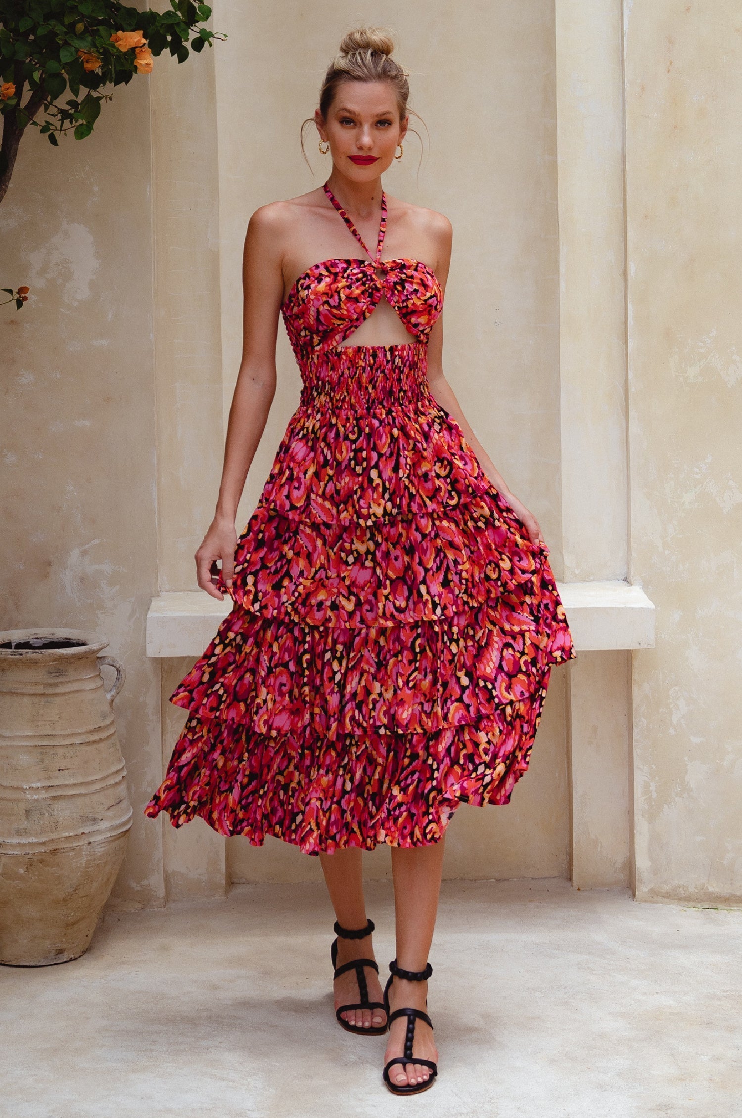 Woman wearing a red floral halter tiered midi dress standing in a decorative setting, front view