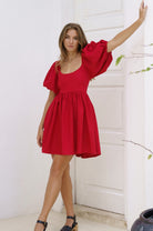 Woman wearing a red mini dress with puffed sleeves against a white background
