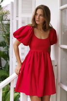 Woman wearing a red dress with puff sleeves standing in a bright outdoor setting.