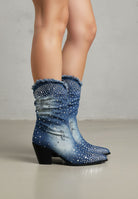 Blue denim boots with rhinestone details worn by a person on a neutral background