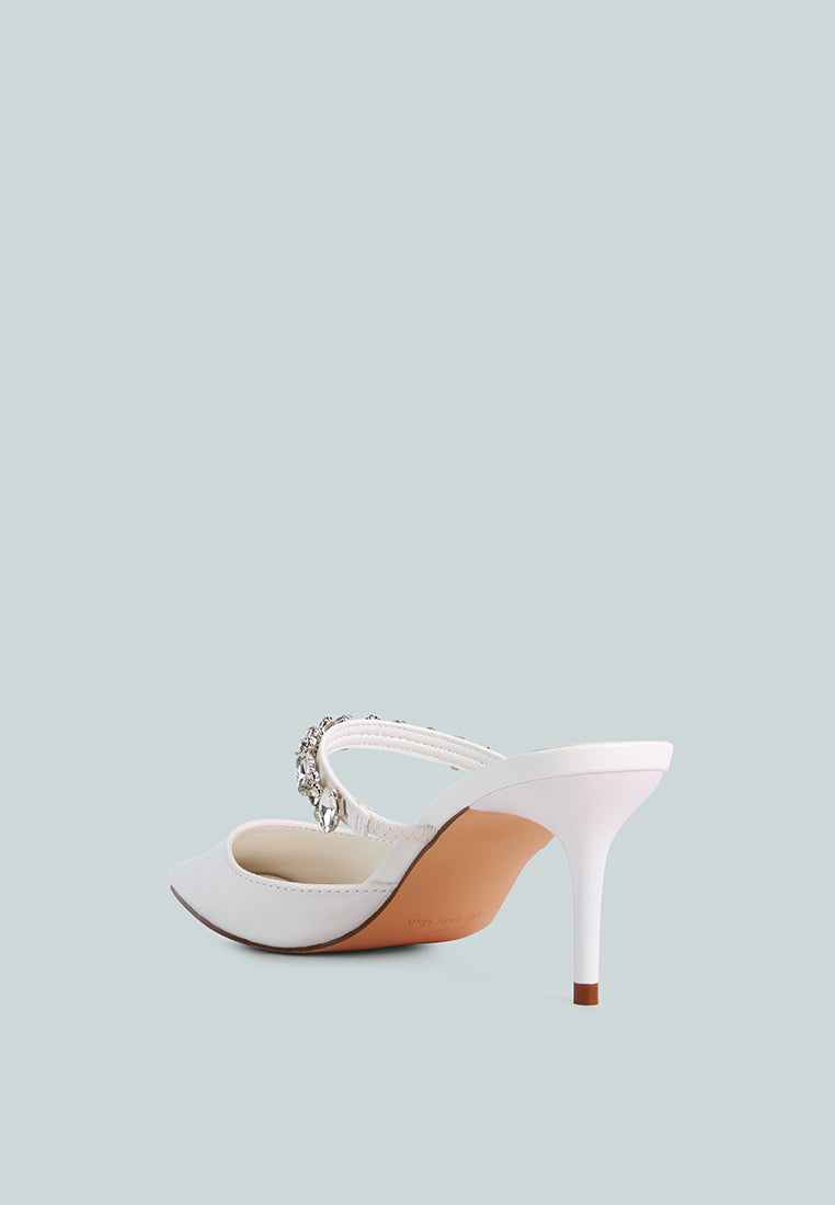 White mid-heeled shoe with a decorative diamante strap across the top on a light blue background, back view