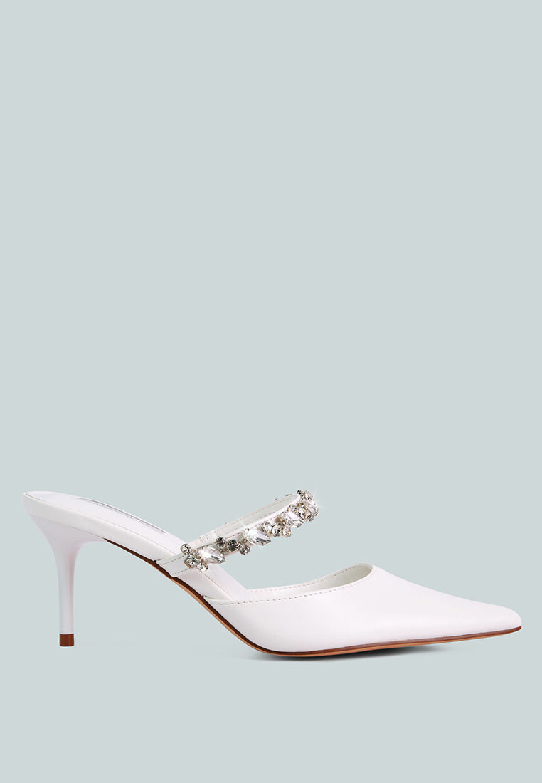 White mid-heeled shoe with a decorative diamante strap across the top on a light blue background, side view