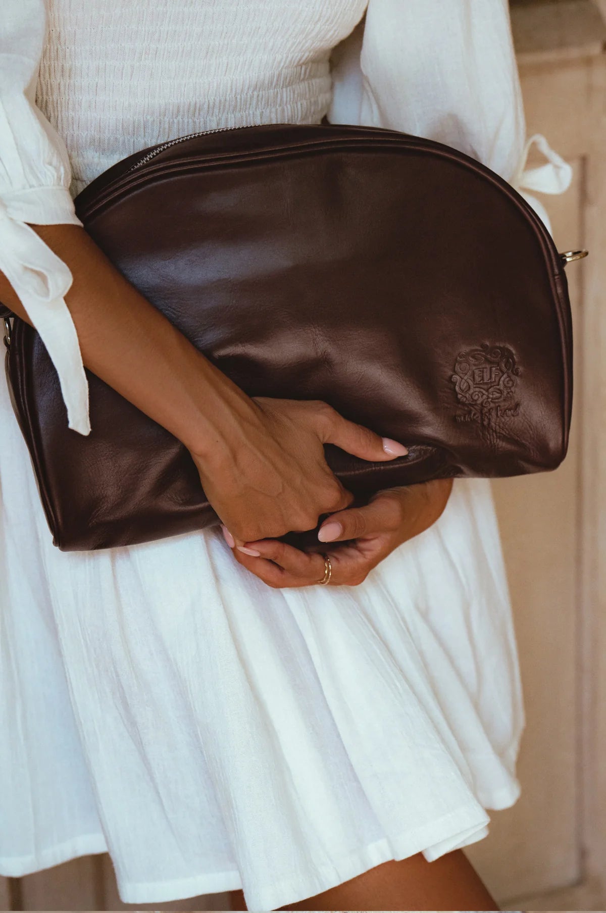 Person holding a brown leather clutch bag with a visible brand logo.