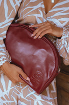 Person holding a maroon leather clutch handbag with a brand logo, wearing a patterned outfit.