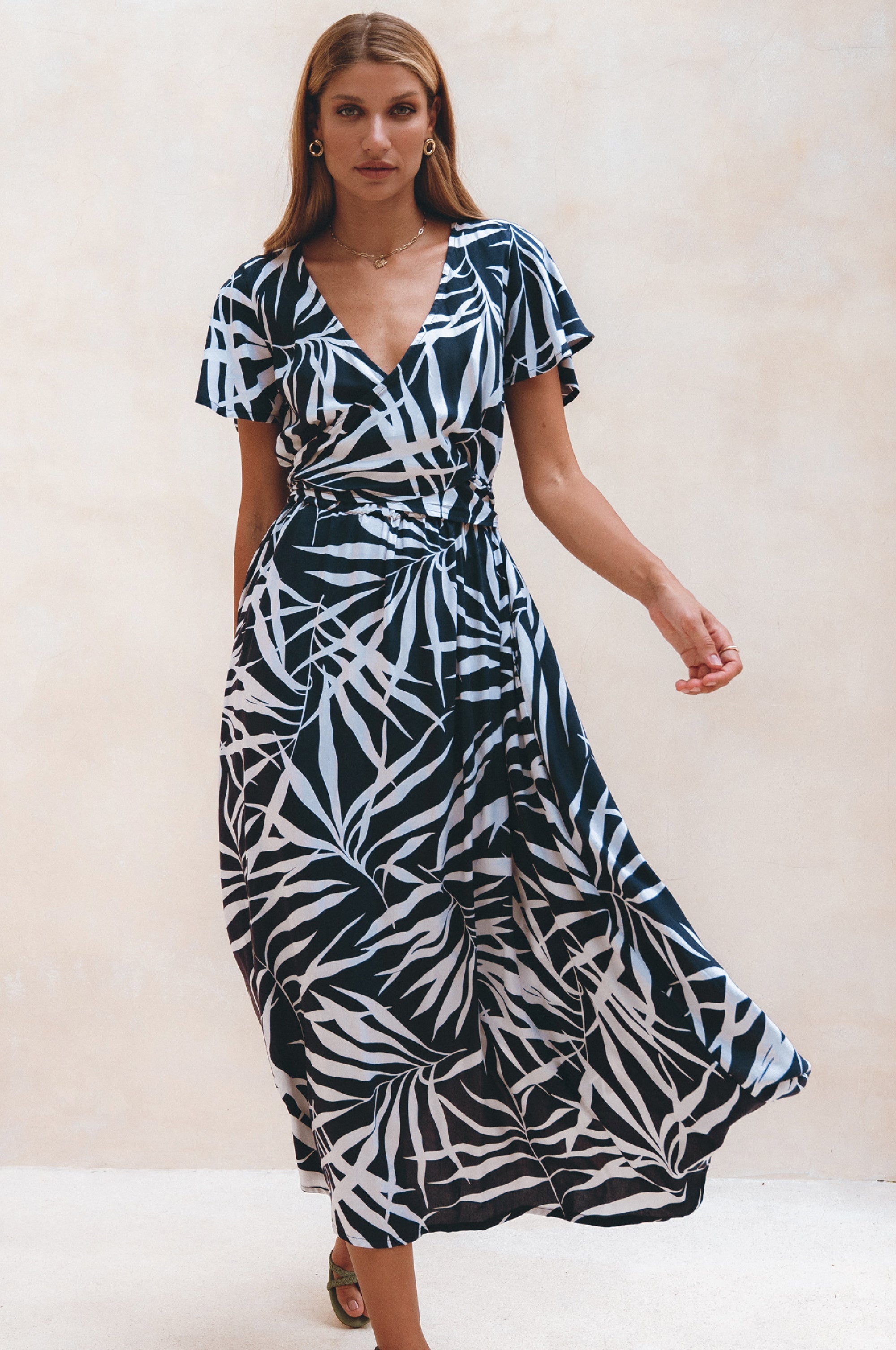 Woman wearing a black and white patterned midi dress with flutter sleeves against a plain background