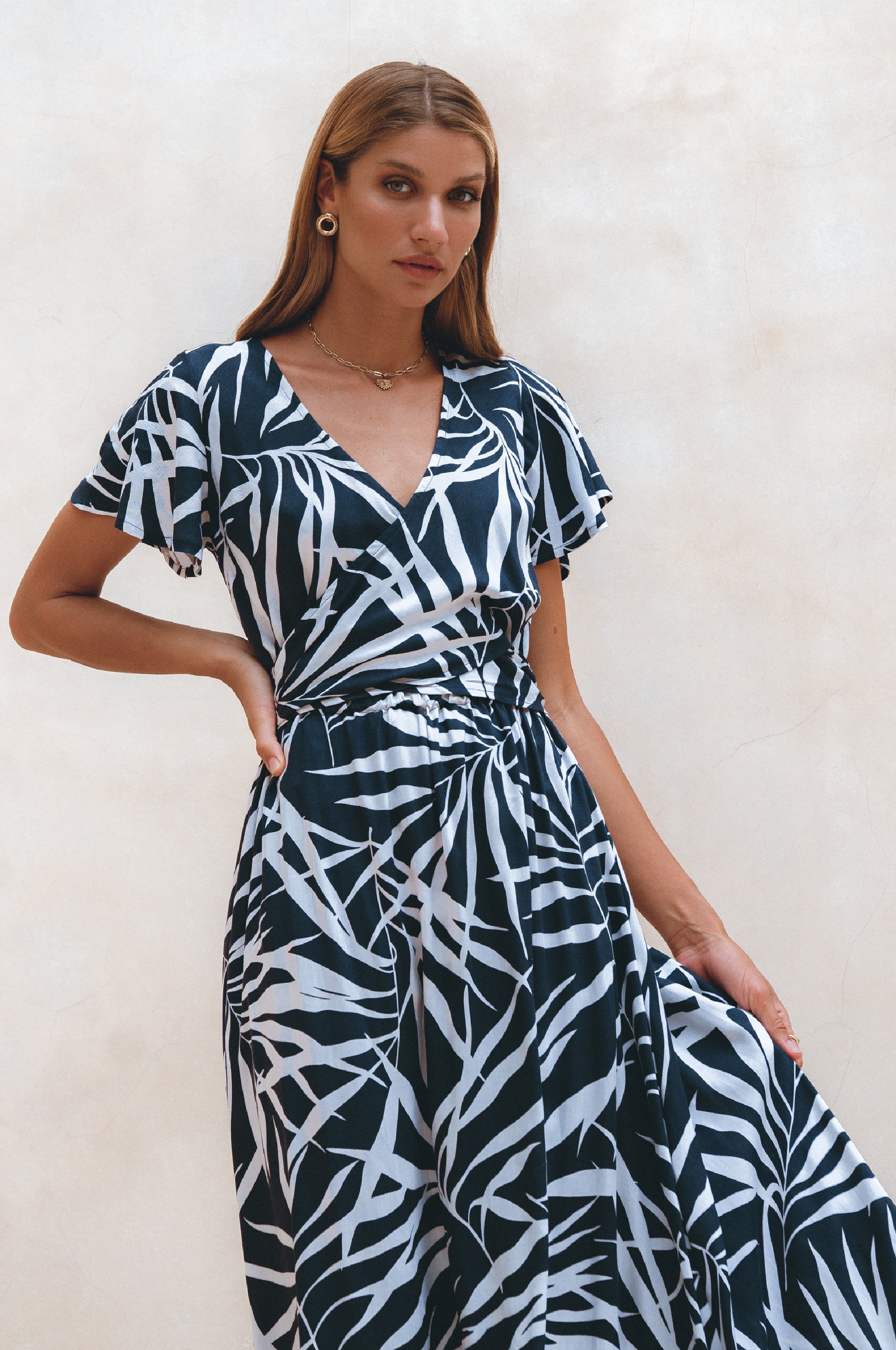 Woman wearing a black and white patterned midi dress in wrap style with flutter sleeves against a light background