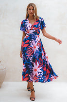 Woman wearing a colorful floral midi dress with flutter sleeves, wrap style against a white background