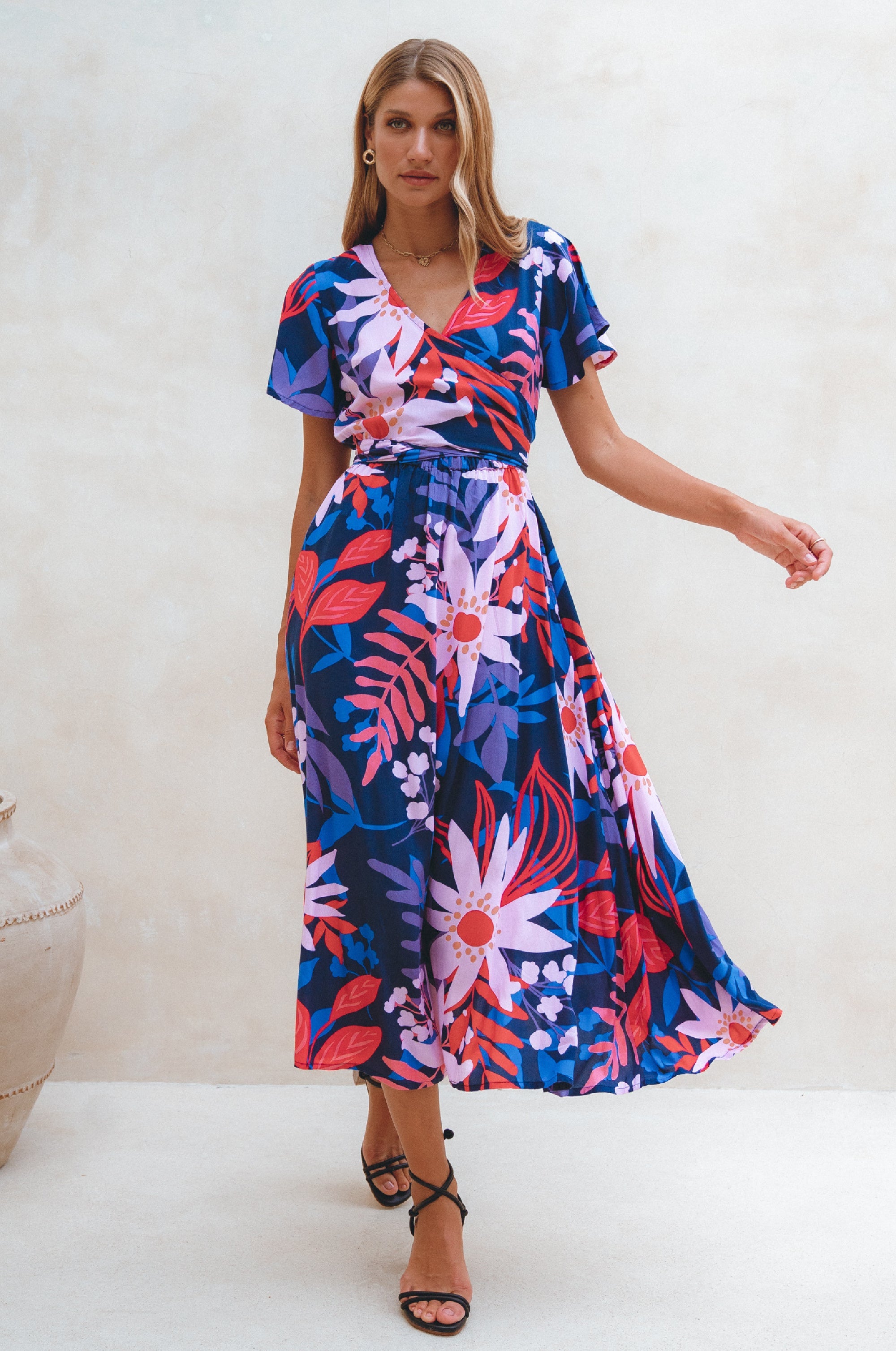 Woman wearing a colorful floral midi dress with flutter sleeves, wrap style against a white background