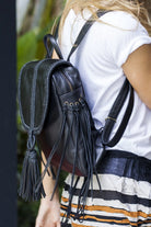 Person wearing a black leather backpack with tassels and fringe