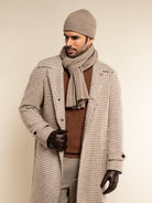 Man wearing a checkered coat, brown sweater, and brown beanie and scarf on a plain background
