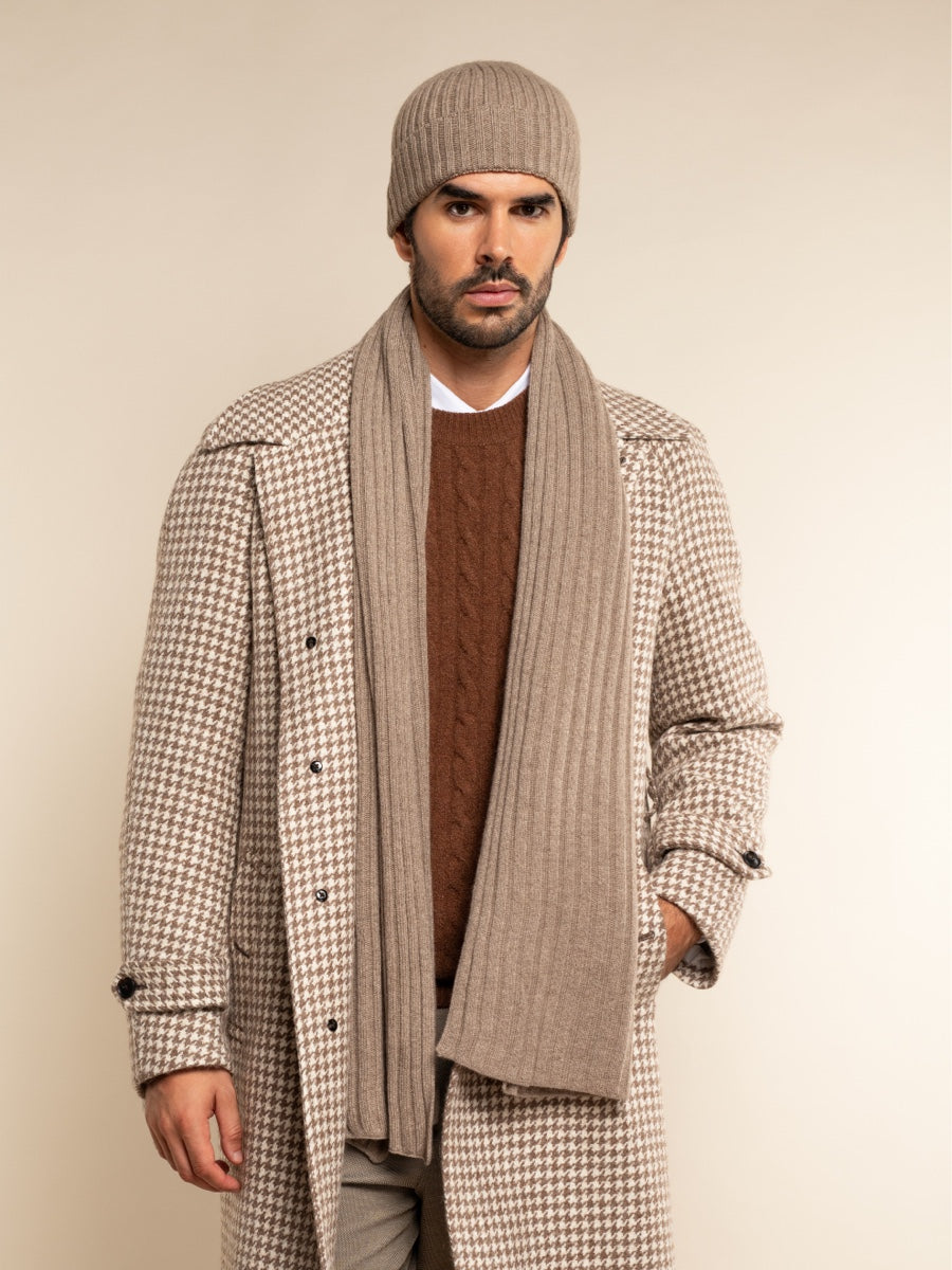 Man wearing a checkered coat, brown sweater, and scarf against a beige background