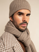 Man wearing a brown knit beanie and scarf against a beige background