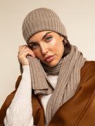 Woman wearing a brown knit beanie and scarf against a beige background