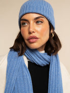 Woman wearing a light blue cashmere knit beanie and scarf against a beige background