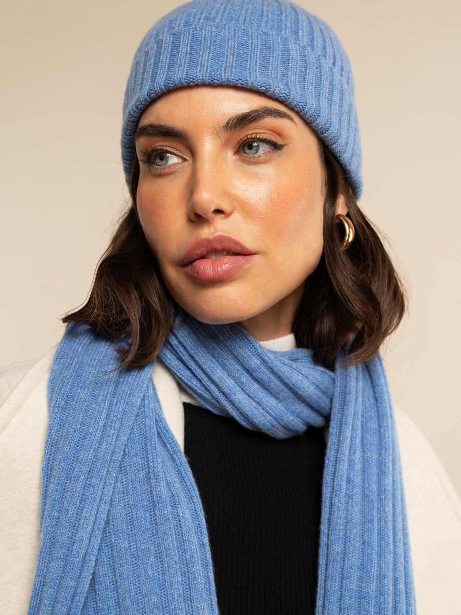 Woman wearing a light blue cashmere knit beanie and scarf against a beige background