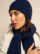 Woman wearing a navy blue cashmere knit beanie and scarf against a beige background