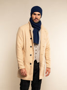Man wearing a beige coat, navy beanie, and scarf against a beige background