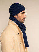 Man wearing a navy beanie and scarf with a beige coat against a beige background