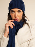 Woman wearing a navy blue knit cashmere hat and scarf against a beige background