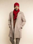 Man wearing a checkered coat, red scarf, and beanie on a beige background