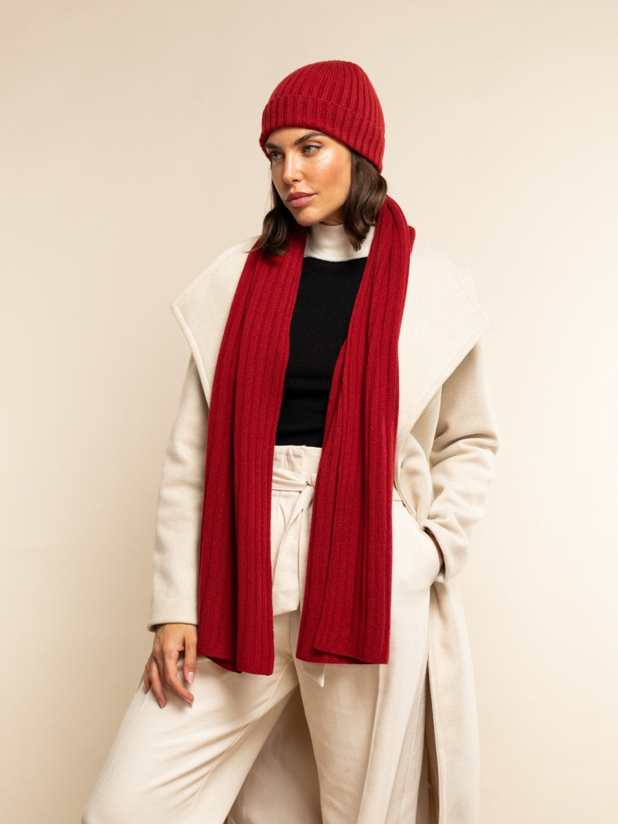 Woman wearing a red cashmere knit beanie and scarf with a beige coat on a beige background